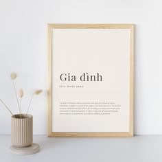 there is a vase with some flowers in it next to a framed poster that says gia dinh