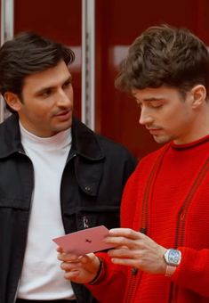 two men standing next to each other looking at an electronic device