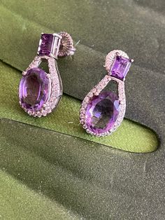 Lovely silver amethyst dangle earrings. Long oval faceted deep purple earring surrounded with white round topazs. Hinged post attached is an emerald cut pronged set amethyst . Marked 925 on the back of each earring. 3 cm in height. 1.5 cm width (measured in middle ). TCW: 11 g. Purple Earring, Gold Rope Chains, Coral Ring, Puffed Heart, Purple Earrings, Silver Dangle Earrings, Earrings Long, Fun Earrings, Silver Earrings Dangle