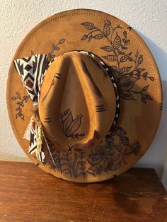 These custom hand burned wide brim western hats features a fabric hand tied band, and feathers. Every hat is customizable free of charge so please reach out to me via message so we can get a beautiful hat made for you. THE HAT PICTURED IS SOLD BUT I CAN MAKE ONE FOR YOU JUST LIKE IT. All designs are on the top of the hat unless otherwise asked. The band color is also customizable, so if you would like a specific color please let me know.  THE HAT LISTED IS CAMEL This hat is NOT a Charlie1Horse hat, and the price reflects that. The hat is 65% cotton 35% polyester. It is a vegan faux suede.  All hats are one size fits most with an adjuster tie on the inside. The hat is 22.8" or 57cm at its largest.  ALL HATS ARE MADE TO ORDER. NO HAT WILL BE 100% THE SAME DUE TO HAND BURNING EACH ONE INDIVID Hand Painted Western Hat Bands For Festival, Bohemian Brown Fedora For Kentucky Derby, Brown Bohemian Fedora For Kentucky Derby, Bohemian Hand Painted Fedora For Country Events, Western Hand Painted Fedora For Country Events, Bohemian Brown Hat Bands For Kentucky Derby, Brown Bohemian Hat Bands For Kentucky Derby, Bohemian Hand-painted Hats For Country Events, Bohemian Wide Brim Hat Bands Hand Painted