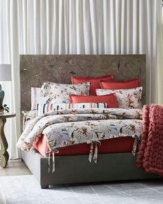 a bed with red and white comforters in a bedroom next to a window covered by curtains