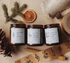 three candles sitting on top of a wooden table next to an orange and pine cone