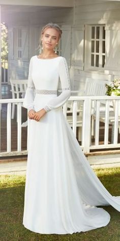 a woman wearing a white wedding dress standing in front of a house with her hands on her hips