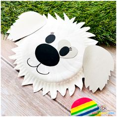 a paper plate shaped like a dog on the ground with grass behind it and a rainbow ball in the foreground