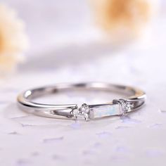 an opal and diamond ring sitting on top of a white table next to flowers