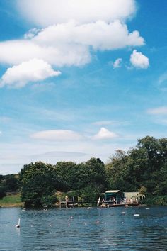 a body of water surrounded by trees and clouds in the blue sky with people on it