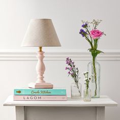 a table topped with books and vases filled with pink flowers next to a lamp