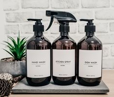 three bottles of hand wash sitting on top of a table next to a potted plant