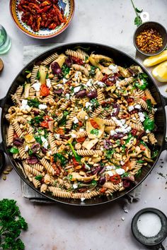 a skillet filled with pasta and vegetables on top of a white counter next to other dishes