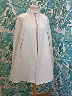 a white coat on a mannequin in front of a floral wallpaper