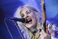 a woman singing into a microphone while holding a guitar