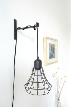 a black lamp hanging from the side of a wall next to a vase with flowers