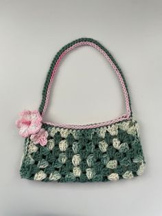 a crocheted purse with a pink flower on the front and green, white, and gray handles