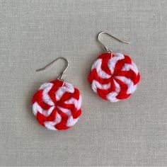 two red and white earrings with silver earwires on a gray surface, one is made from yarn