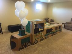 a cardboard train with balloons on top in a living room next to a couch and chair