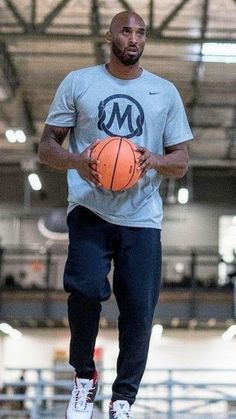 a man holding a basketball while standing on top of a gym floor with other people