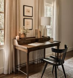 a desk with a lamp, chair and pictures on the wall behind it in front of a window