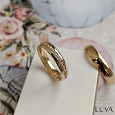 two gold wedding rings sitting on top of a white box next to a flowered wall