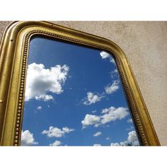 a gold framed mirror reflecting the sky and clouds