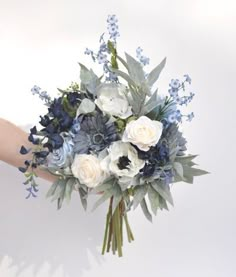 a bouquet of white and blue flowers is held by someone's hand in front of the camera