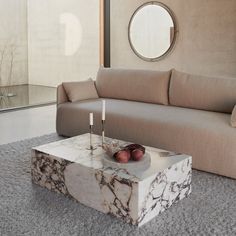 a marble coffee table with candles and fruit on it in front of a beige couch