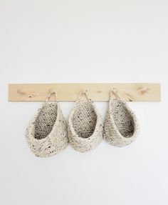 three baskets hanging from a wooden hook on a white wall with two pairs of shoes in them