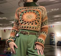 a woman wearing green pants and a crocheted sweater with an orange flower on it