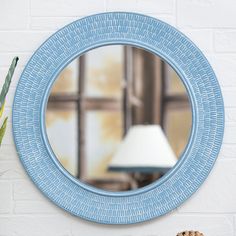 a round blue mirror hanging on the wall next to a table with a lamp and potted plant