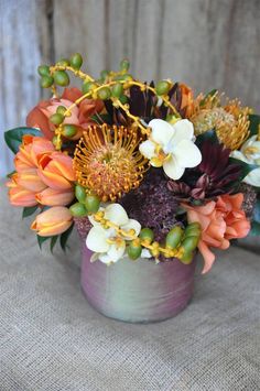 a vase filled with lots of flowers on top of a cloth covered table next to a wooden wall