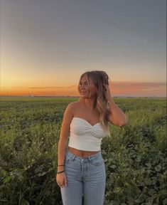 a woman standing in the middle of a field with her hand on her head and looking off to the side