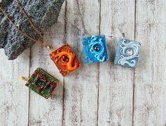 four different colored square pendants on a white wooden surface with a rock in the background