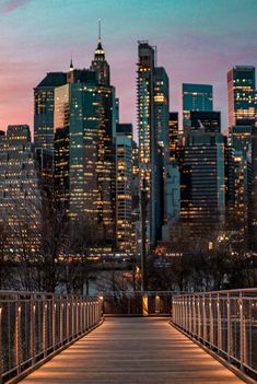 the city skyline is lit up at night, and there are benches on the walkway