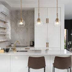 two bar stools sit in front of an island with marble countertops and white cabinets