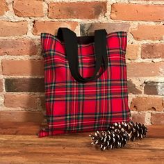 a red and black plaid tote bag next to a pine cone on a wooden table