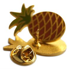 a pin with a pineapple on it sitting next to a pair of gold cufflinks