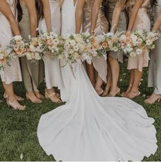 a group of women standing next to each other in front of a white dress holding bouquets