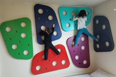 two people climbing up and down the side of a wall made out of plastic pegs