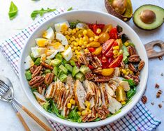 a white bowl filled with chicken, vegetables and hard boiled eggs on top of a checkered table cloth