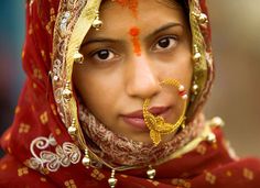 a woman wearing a red and gold headdress with an orange nose ring on her forehead