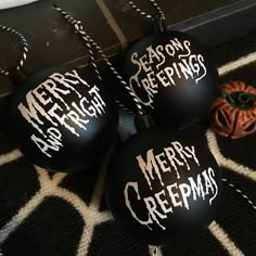 three black ornaments with merry greetings written on them sitting on the floor next to a pumpkin