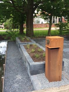 a wooden trash can sitting in the middle of a graveled area next to trees