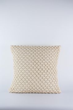 a white pillow sitting on top of a white floor next to a wall with a light colored background