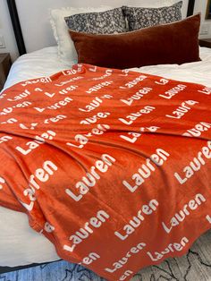 an orange blanket is on top of a white bed with pillows and blankets around it