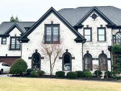 a white car is parked in front of a large brick house with black shutters