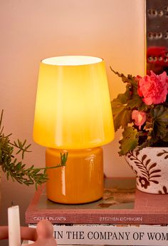 a yellow lamp sitting on top of a table next to books and a potted plant