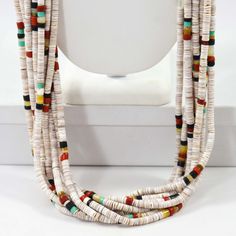 Collier à dix brins avec perles Heishi roulées à la main en coquillage blanc, corail méditerranéen, jais et turquoise. Ce collier présente un support enveloppant traditionnel de la joaillière de Saint-Domingue, Mary Frances Coriz. May Frances Coriz, alias Mary Coriz Aguilar, est issue d'une famille incroyablement talentueuse et est la fille de Mary Lovato et la sœur d'Anthony Lovato. Mary est mariée à John Aguilar qui est également un bijoutier talentueux.

 Nombre de brins : 10
 Longueur du collier : 32" White Heishi Beads Artisan Jewelry, White Artisan Heishi Bead Jewelry, Artisan Multi-strand Jewelry With Spacer Beads, White Heishi Beads Necklaces Hand-strung, White Heishi Beads Hand-strung Necklaces, Hand-strung White Heishi Bead Necklaces, White Hand-strung Heishi Bead Necklaces, Hand-strung White Multi-strand Necklace, White Hand-strung Rondelle Necklace