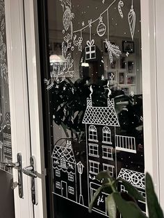 a black and white photo of a window with christmas decorations drawn on the glass, next to a potted plant