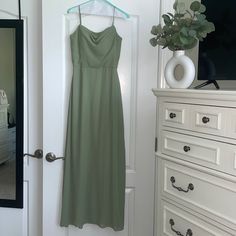 a green dress hanging on a white door in front of a dresser with drawers and a mirror