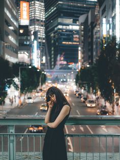 a woman is standing on the sidewalk talking on her cell phone while looking down at the street