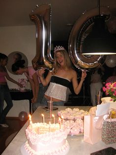 a woman holding up two large balloons in front of a table with cakes and cupcakes